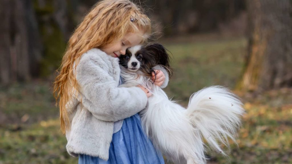 Little girl giving papillon dog a hug while in the park